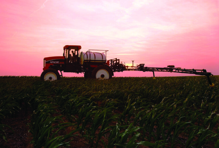 used apache sprayer being used in field with pink sunset in background